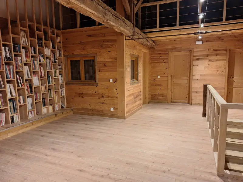 Pièce habillée de bois clair : bibliothèque montée sur mesure du sol au plafond, portes et cloisons en bois, sol stratifié.