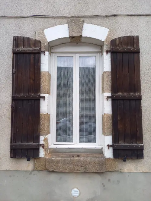 Volets de bois sombres et abîmés, ouverts de part et d’autre d’une fenêtre.